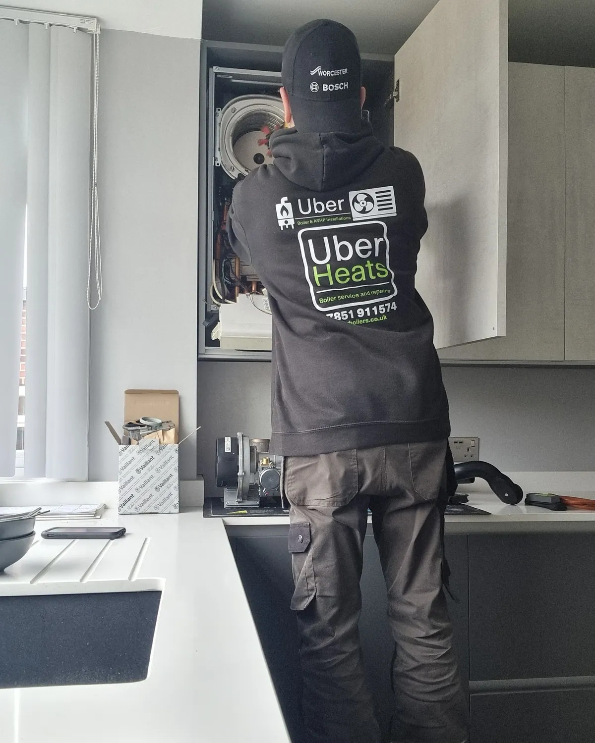 UberHeats engineer servicing a boiler fitted in a kitchen cupboard