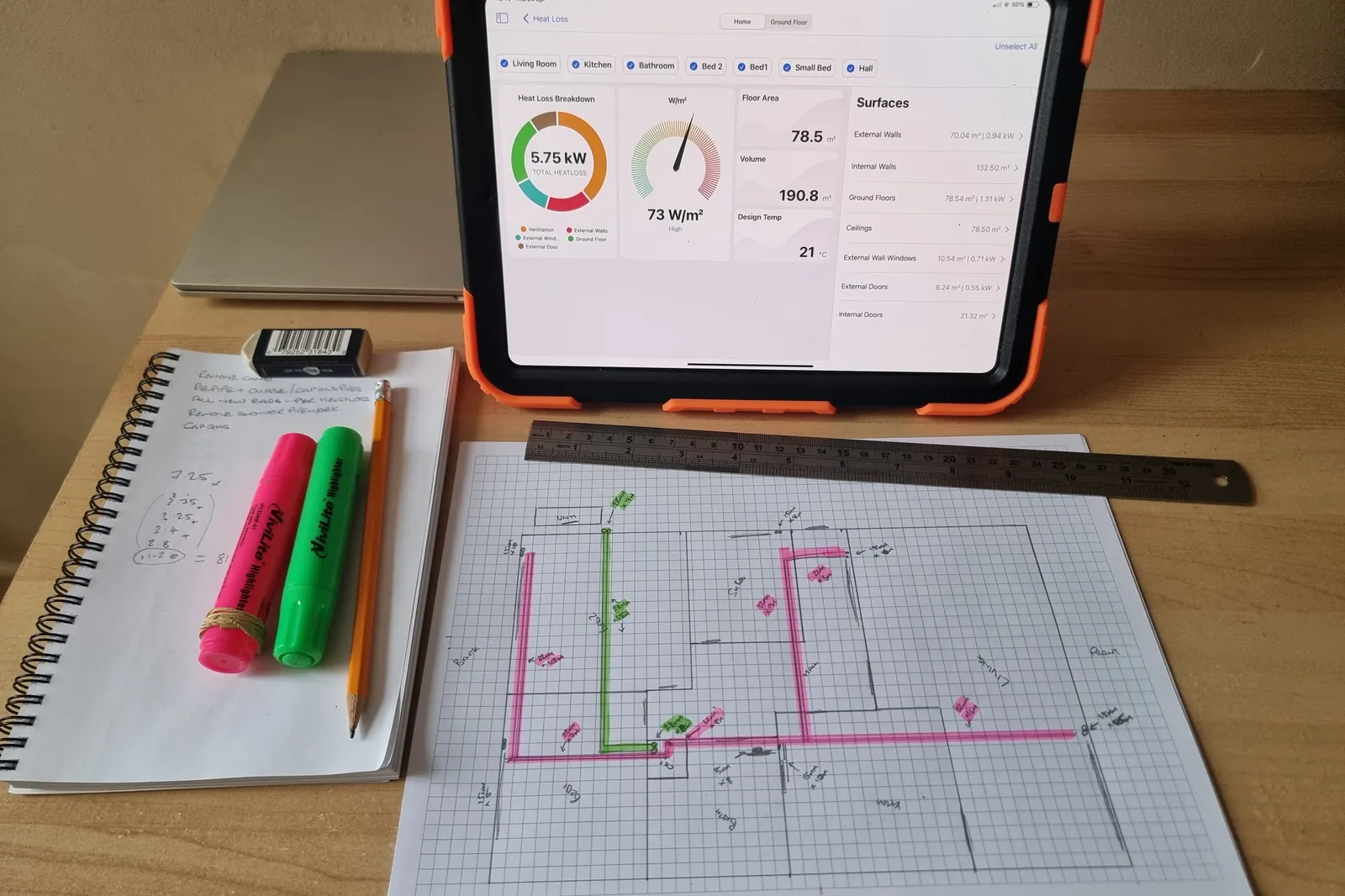 Room-by-room heat loss calculation on an iPad beside system design drawings