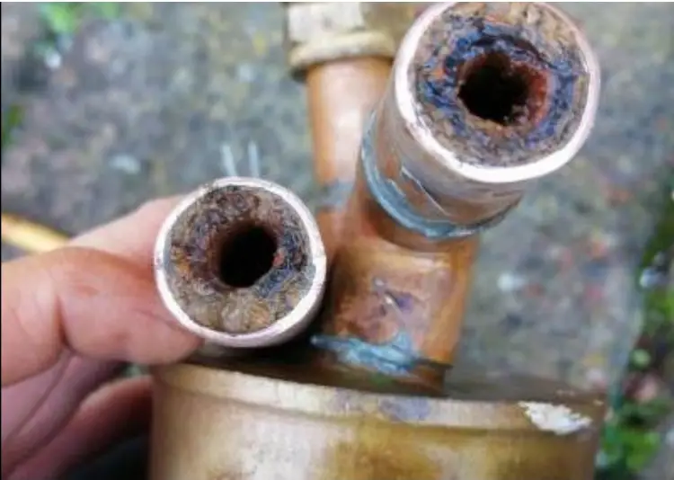 Two heating pipes cut open, their insides narrowed by rust and black sludge